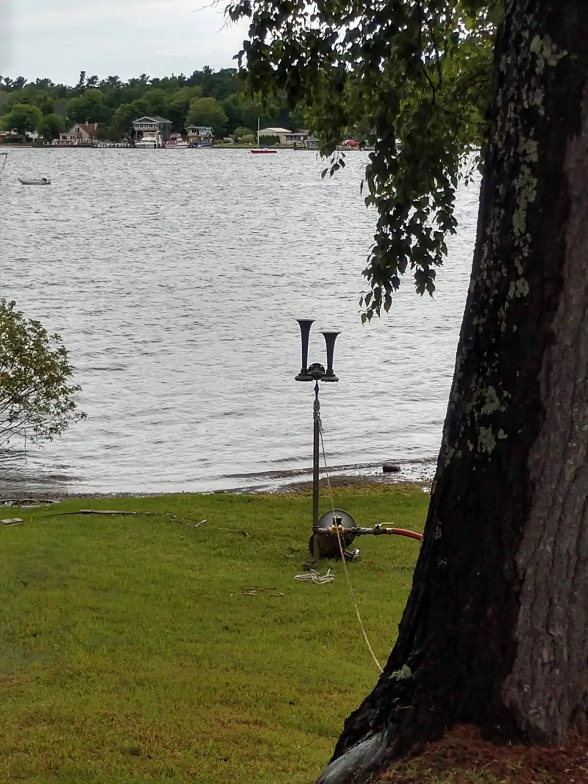 A dual-trumpet air horn and compressor stand on a lawn beside the water.