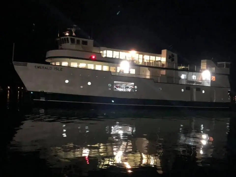 An illuminated ferry moves across dark water, its lights mirrored in rippling reflections.