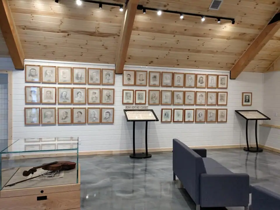 Interior exhibit room with framed portraits, display cases, interpretive panels, and a violin.