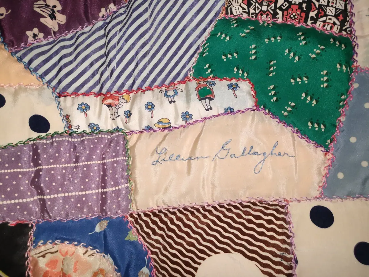 Close-up of a colorful patchwork quilt with patterned fabric pieces and an embroidered name.