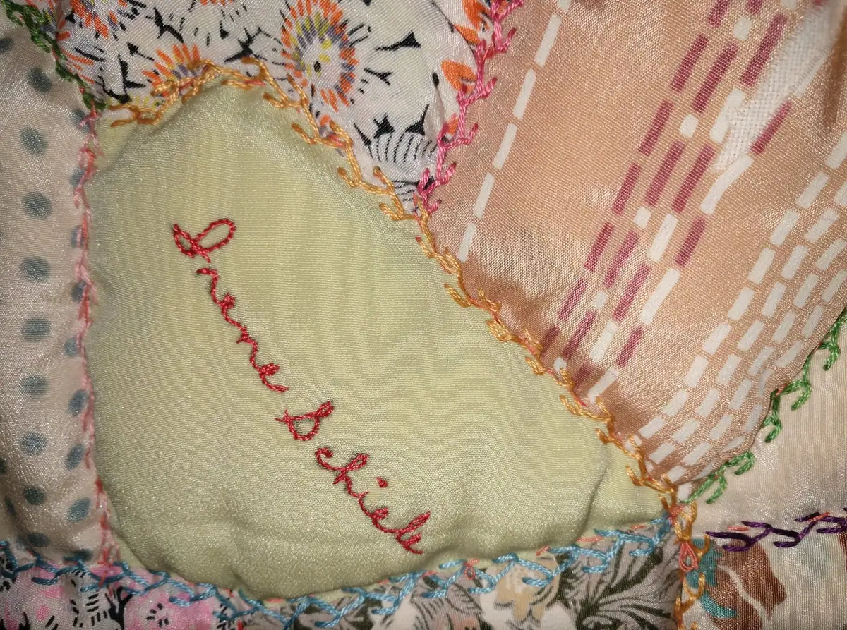 Close-up of a colorful patchwork quilt with embroidered lettering and patterned fabric squares.