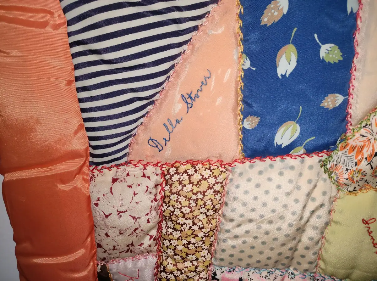 Close-up photograph of a colorful patchwork quilt with floral, striped, dotted, and solid fabric pieces.