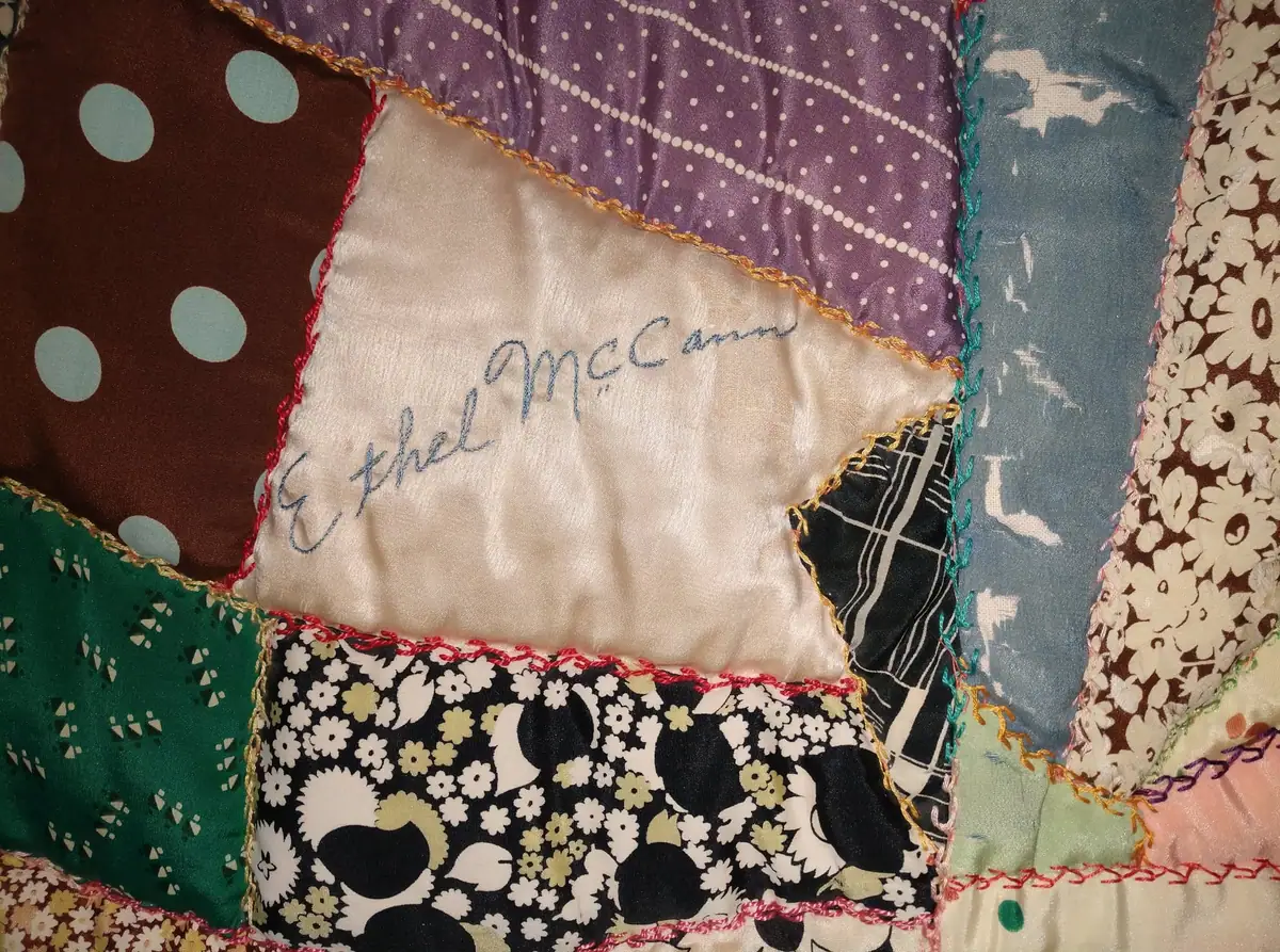 Close view of a patchwork quilt with a handwritten name stitched onto a pale fabric patch.