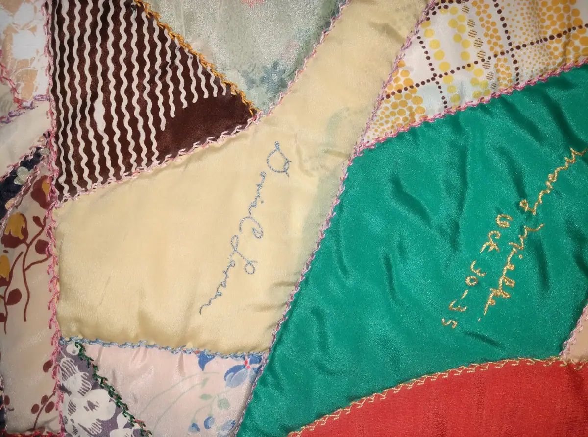 Close-up of a colorful patchwork textile with embroidered lettering and decorative stitched edges.
