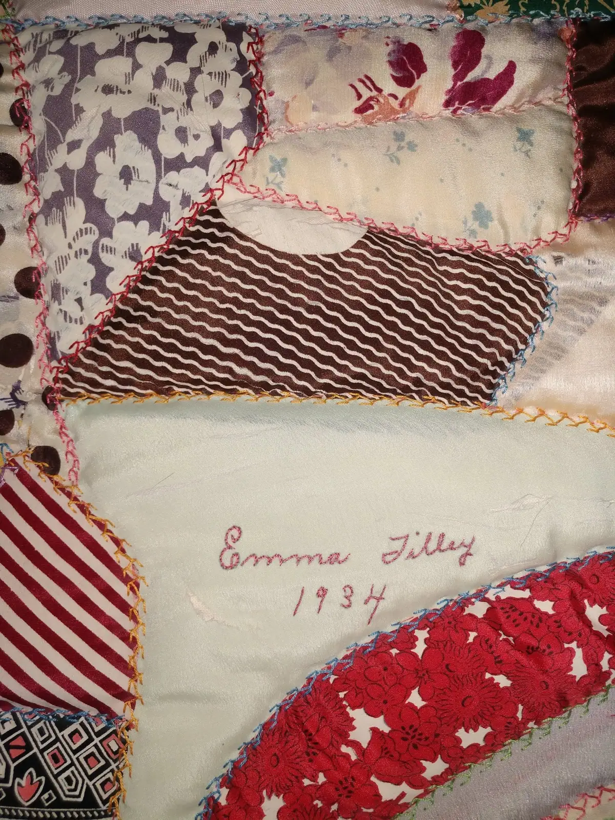 Close-up of a hand-stitched patchwork quilt with patterned fabric pieces and embroidered handwriting.