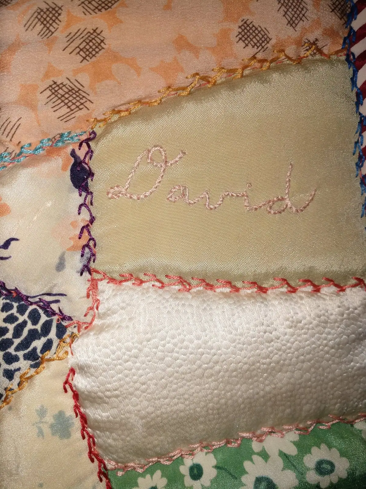 Close-up photograph of a patchwork textile with colorful stitched borders and embroidered cursive lettering.