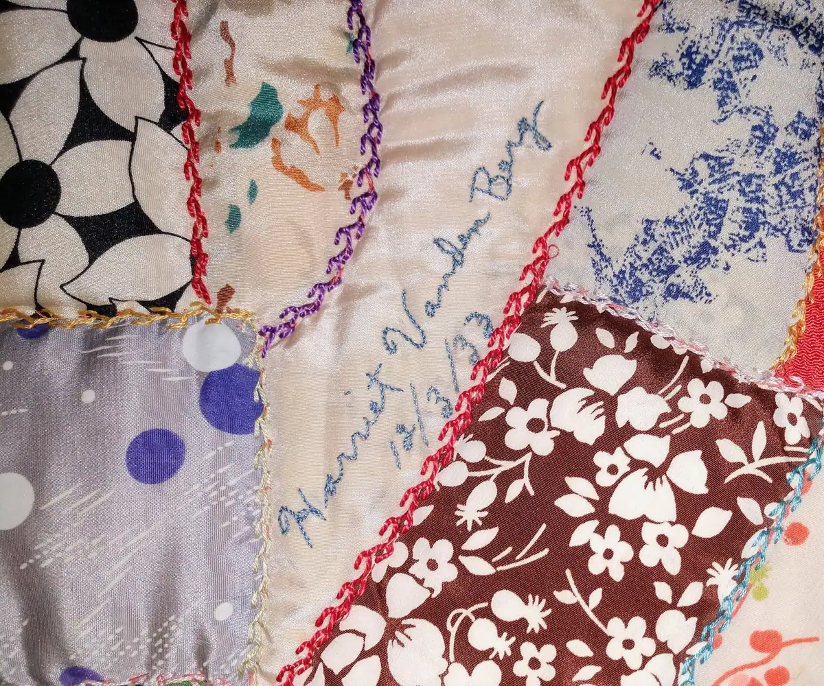 Close-up of a colorful patchwork textile with embroidered seams and floral, geometric, and polka-dot fabrics.
