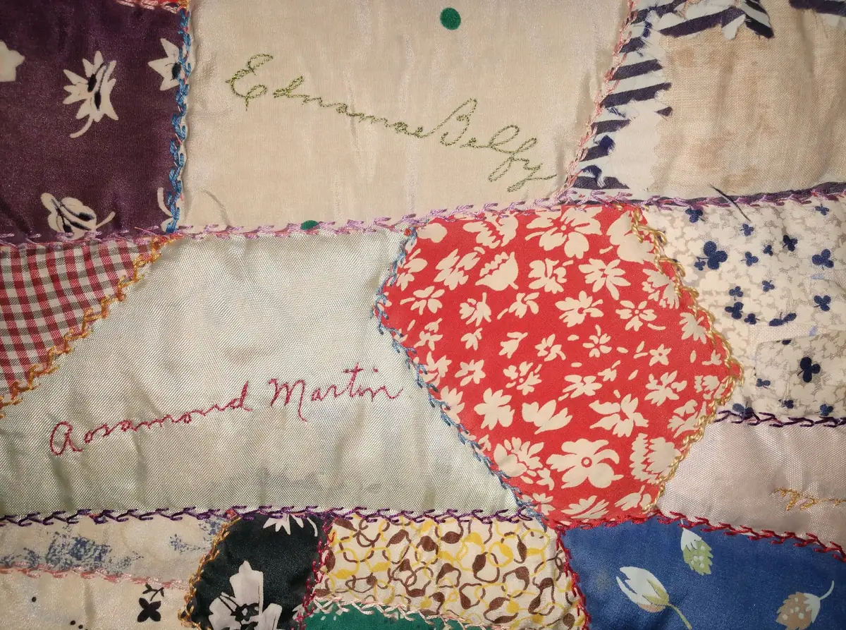 Close-up of a colorful patchwork quilt with floral fabric pieces and embroidered names.