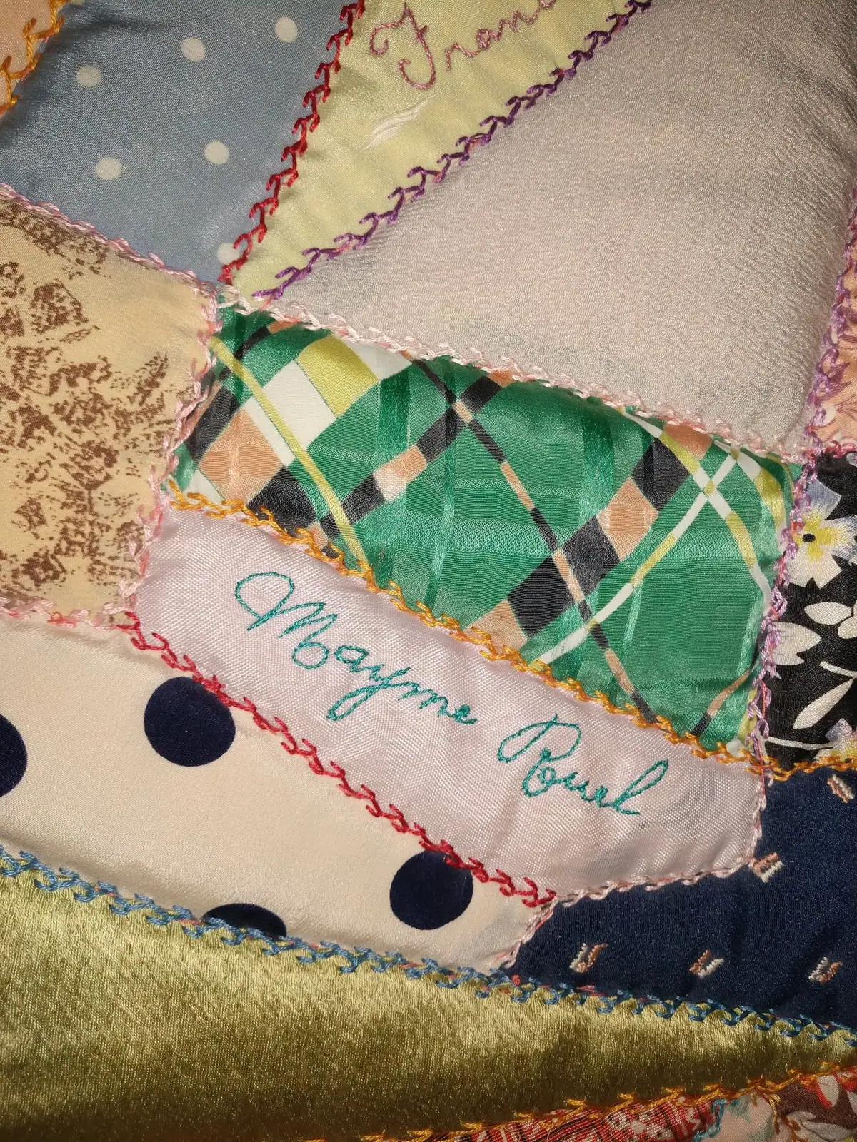 Close-up photograph of a colorful patchwork quilt with patterned fabric pieces and embroidered edging.
