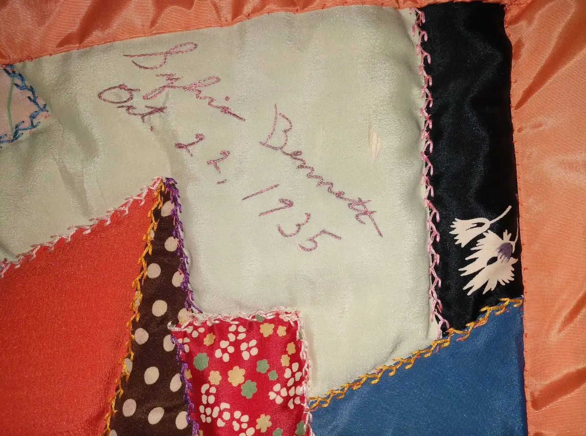 Close-up of a colorful patchwork quilt with embroidered writing and decorative stitched edging.