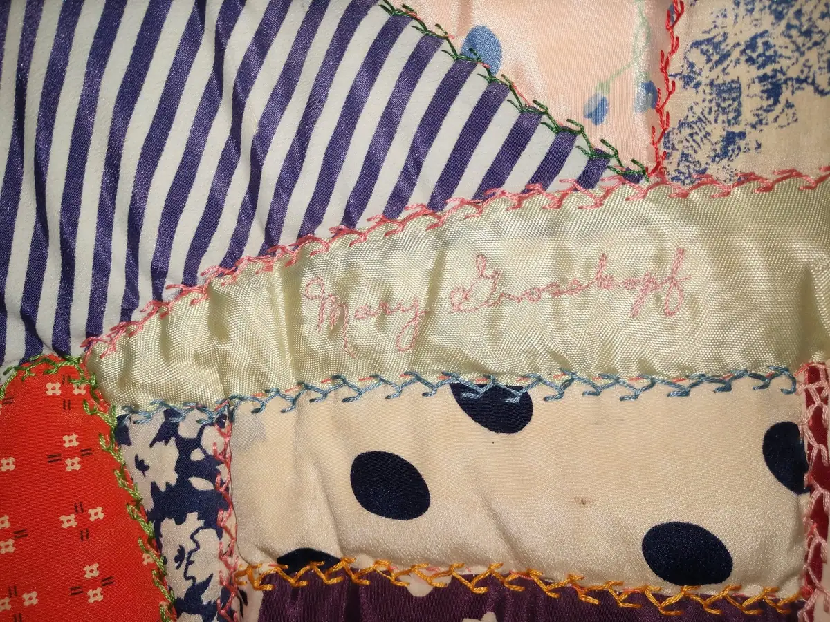 Close-up of a colorful patchwork quilt with embroidered cursive lettering and decorative stitching.