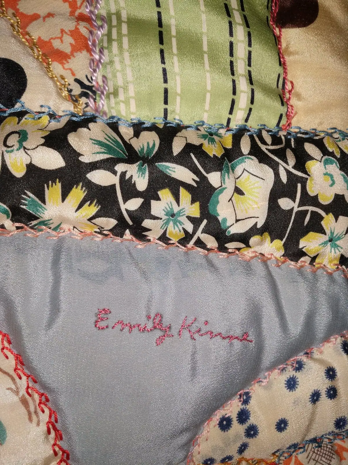 Close-up of a patchwork quilt with colorful fabric panels and the embroidered name “Emily Kinne.”