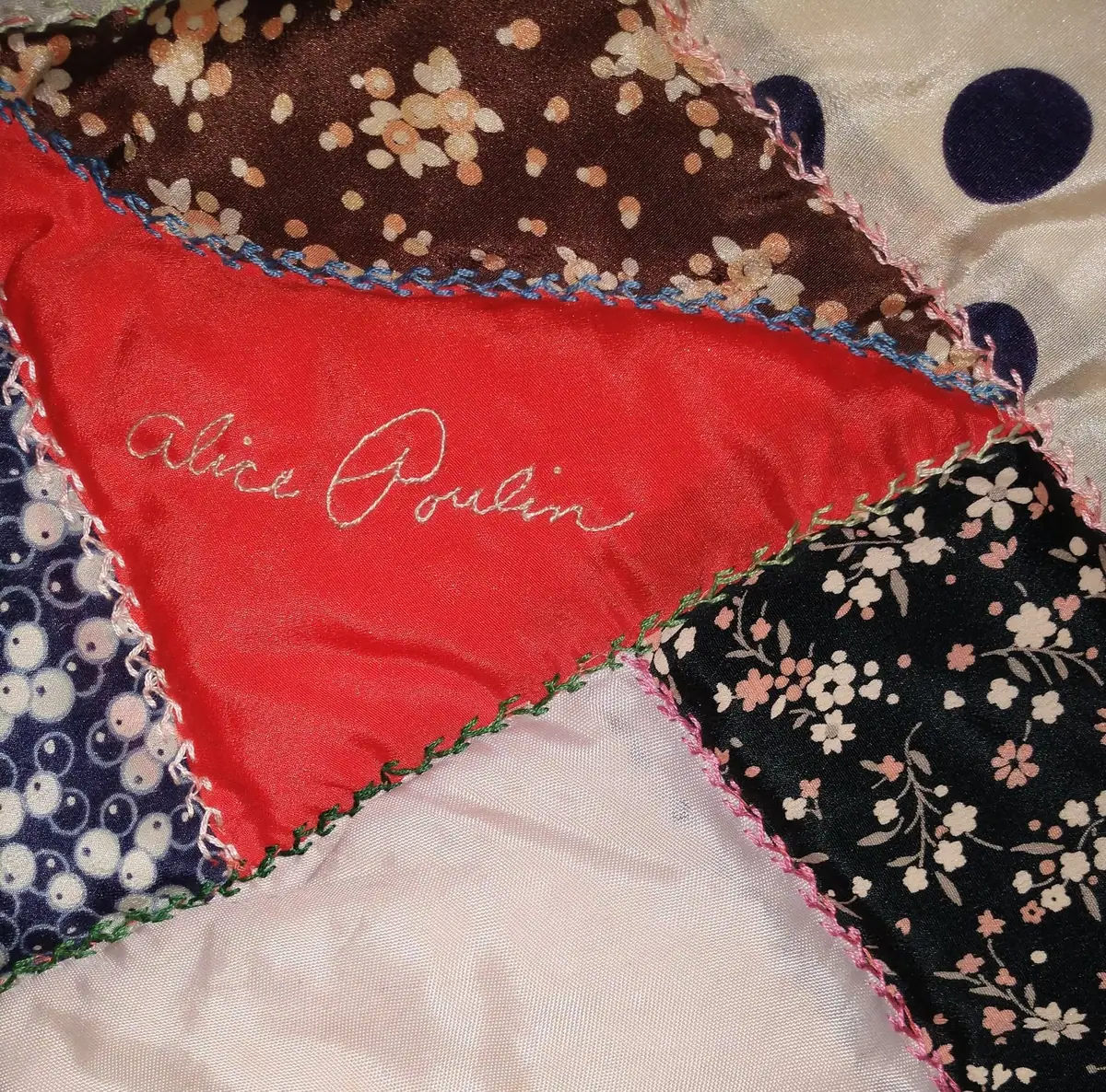 Close-up photograph of a floral patchwork quilt with the name “Alice Poulin” embroidered on a red panel.