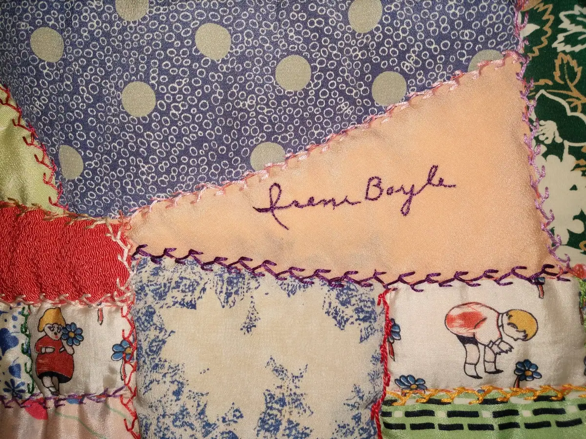 Close-up of a colorful patchwork quilt with embroidered lettering and printed floral and figure motifs.