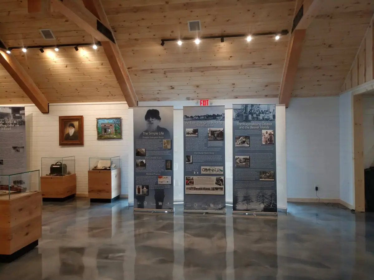 A wood-ceilinged gallery displays interpretive panels, cases, and a framed portrait.