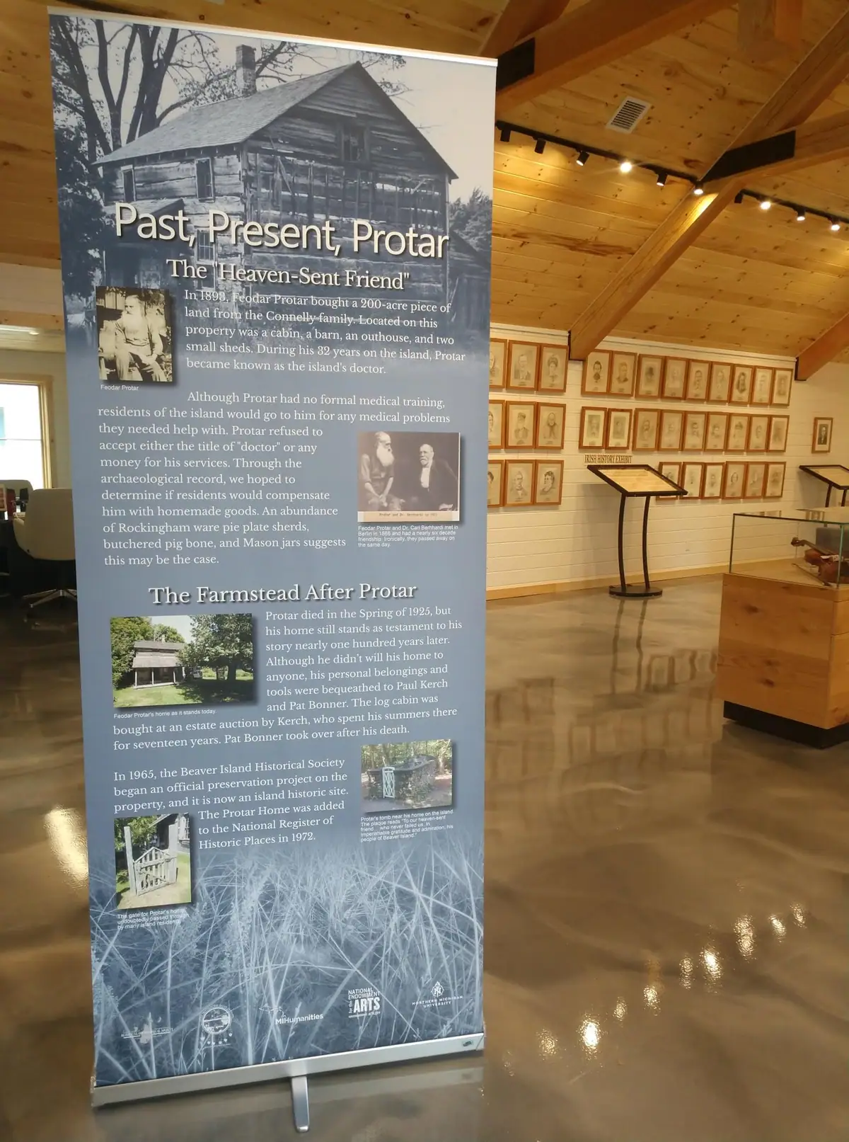 A wood-paneled exhibit room with a large interpretive banner and rows of framed portraits.