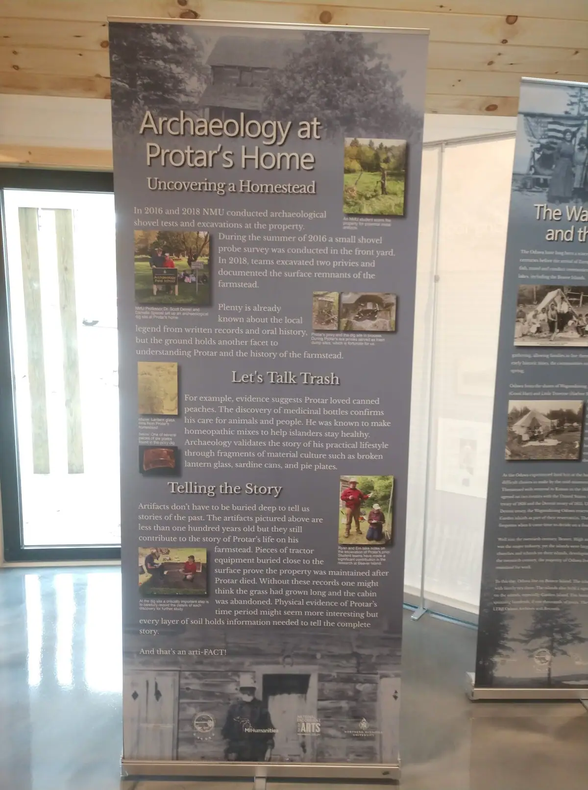 A museum exhibit banner about archaeology at Protar's Home stands beside another historical display panel.