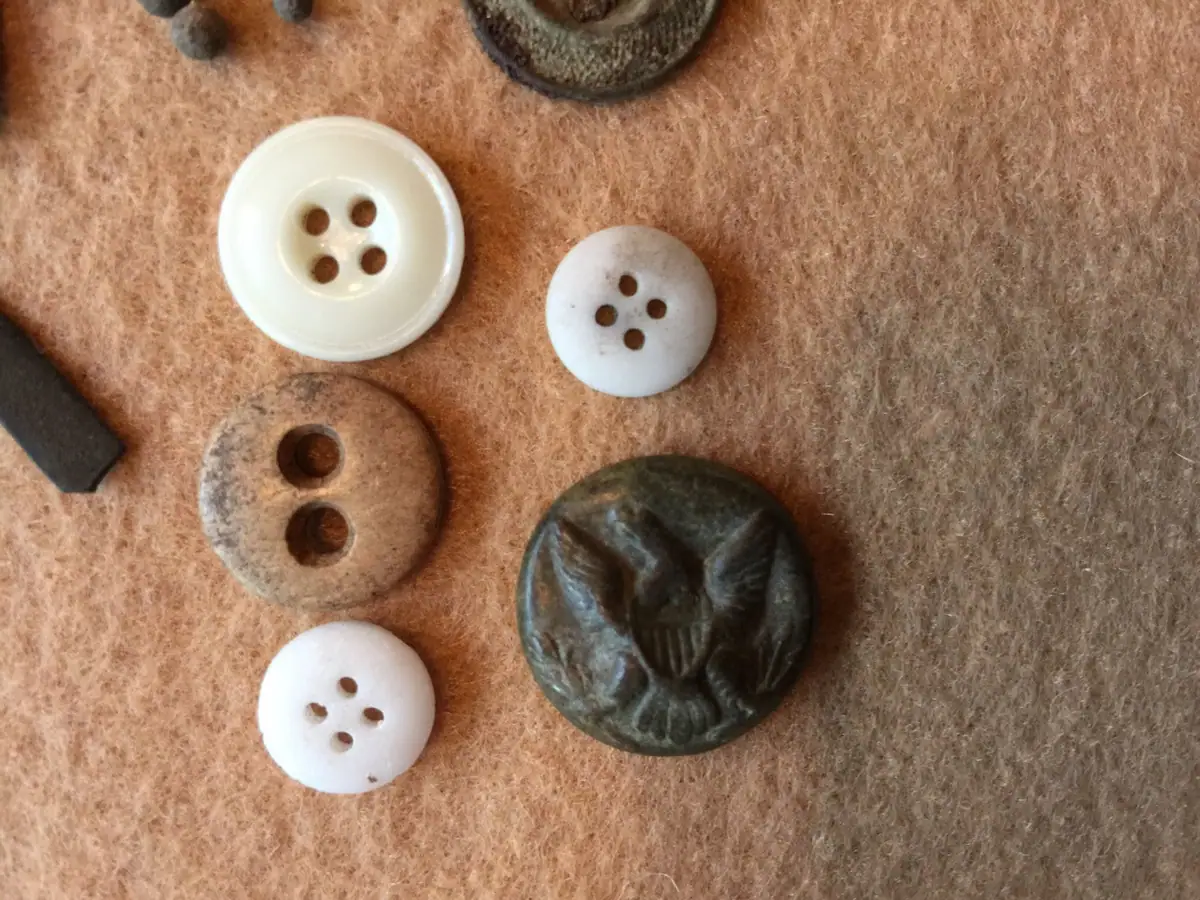 Buttons and fabric scraps arranged on brown felt, including a dark embossed button with an eagle design.