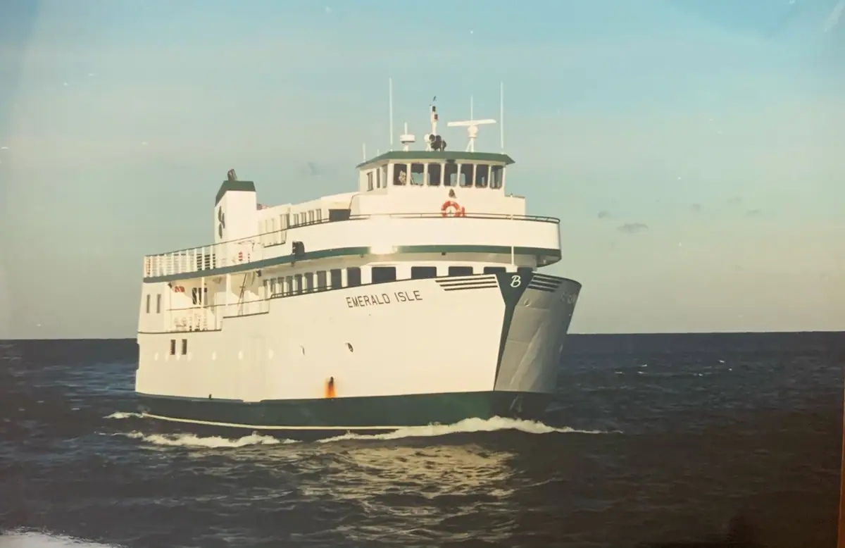 A multi-deck white ferry with a dark hull travels through choppy water beneath a pale sky.