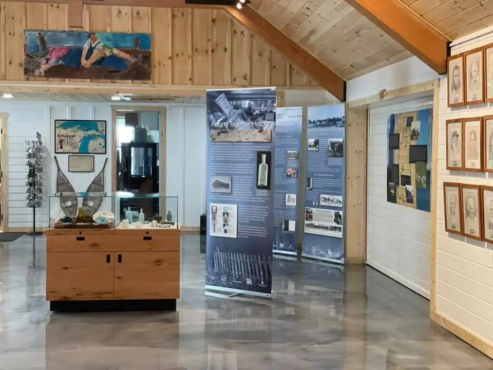Wood-paneled gallery with display cases, interpretive banners, framed portraits, and historical objects.