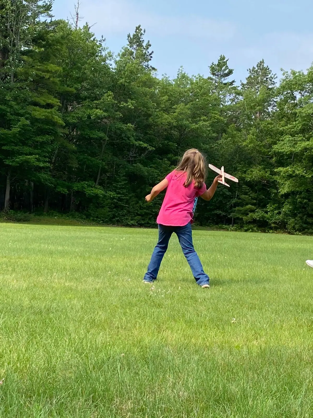 A child runs across a grassy field while holding a small model airplane.