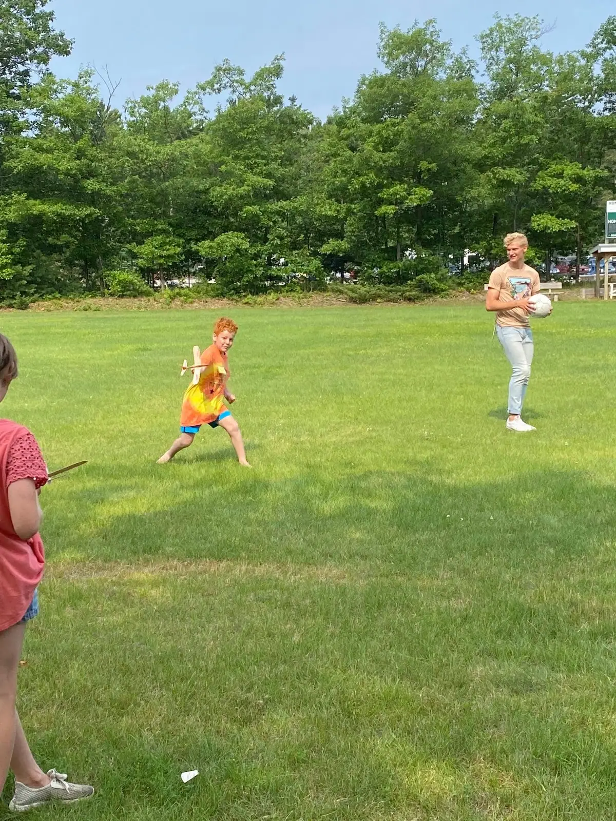 Children play with a toy airplane and soccer ball in a grassy field.