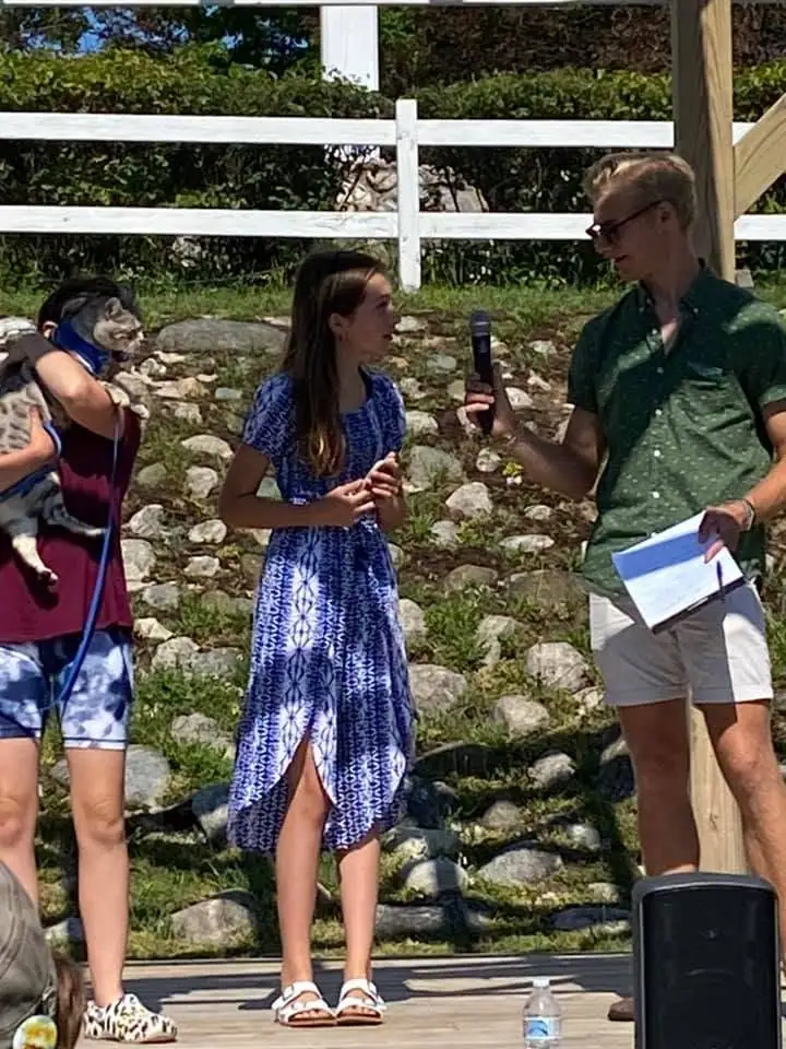 Three people stand outdoors as one holds a microphone and another holds a dog.