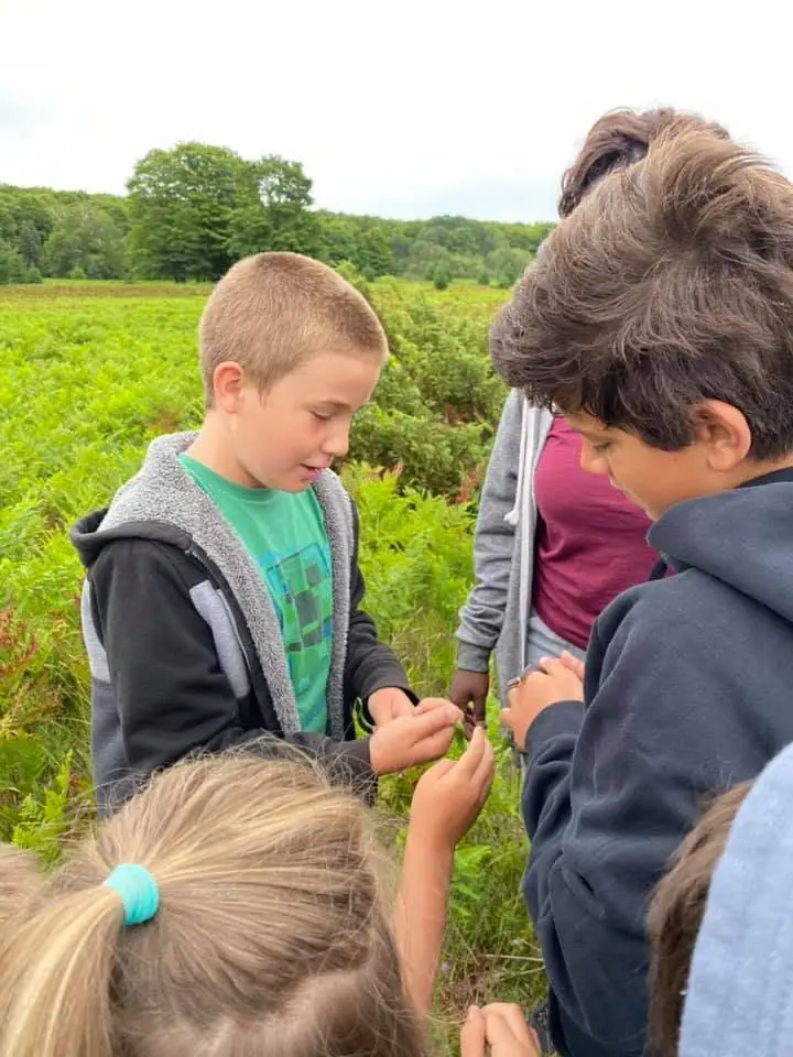 Several children gather in a green field to examine a small object held between them.