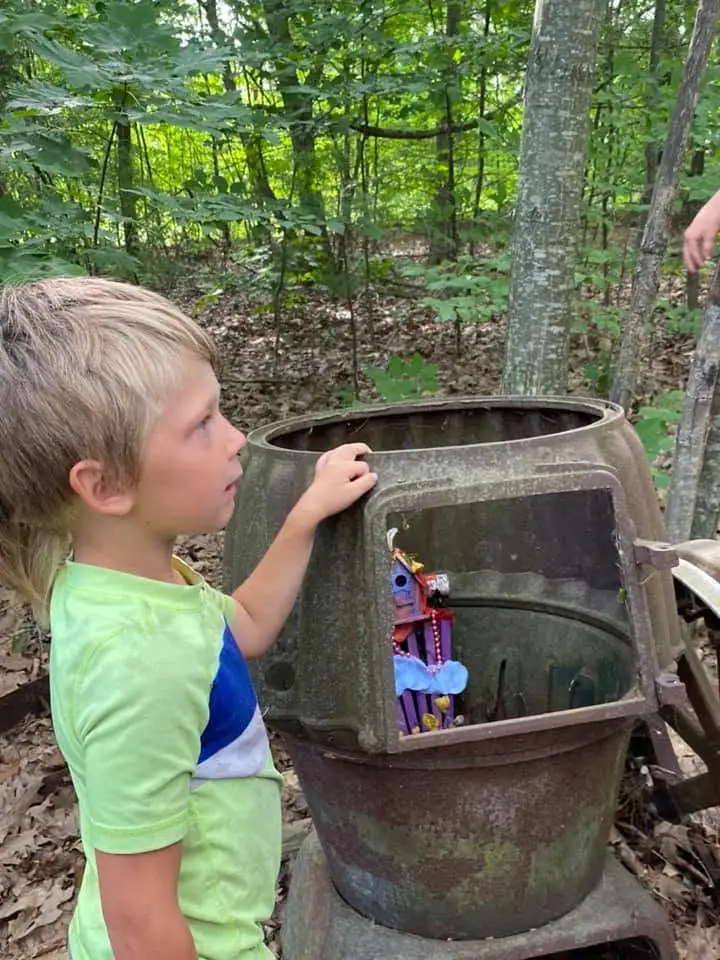 Child examining a decorated metal barrel in a wooded setting.
