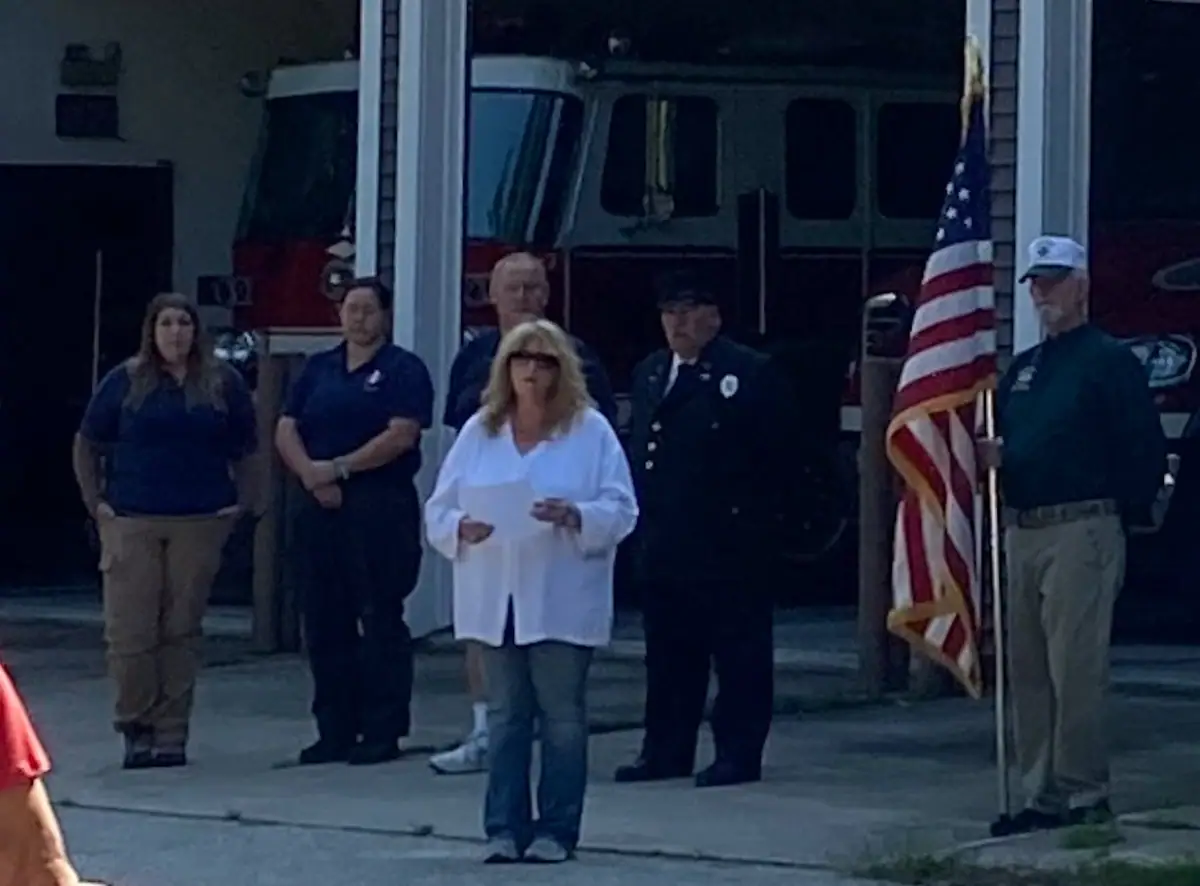 Six people stand outside a fire station beside a fire truck and an American flag.