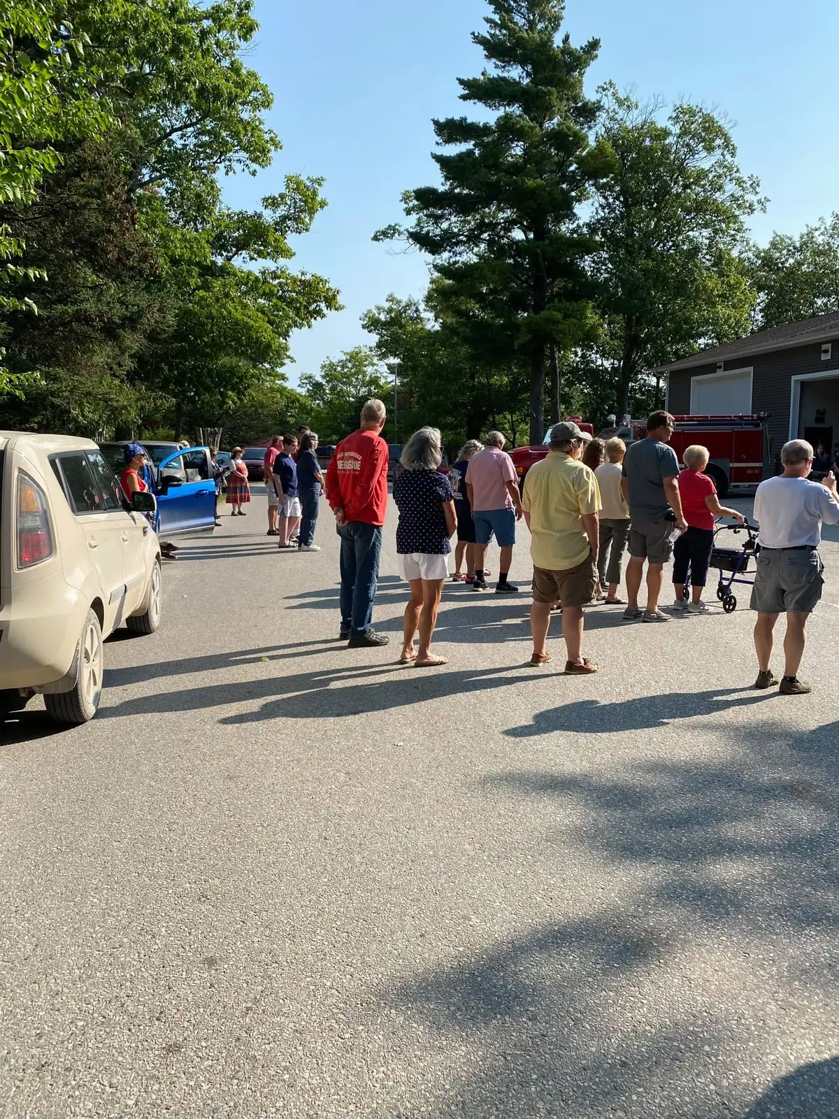 A group gathers beside a red fire truck and garage building in a paved outdoor area.