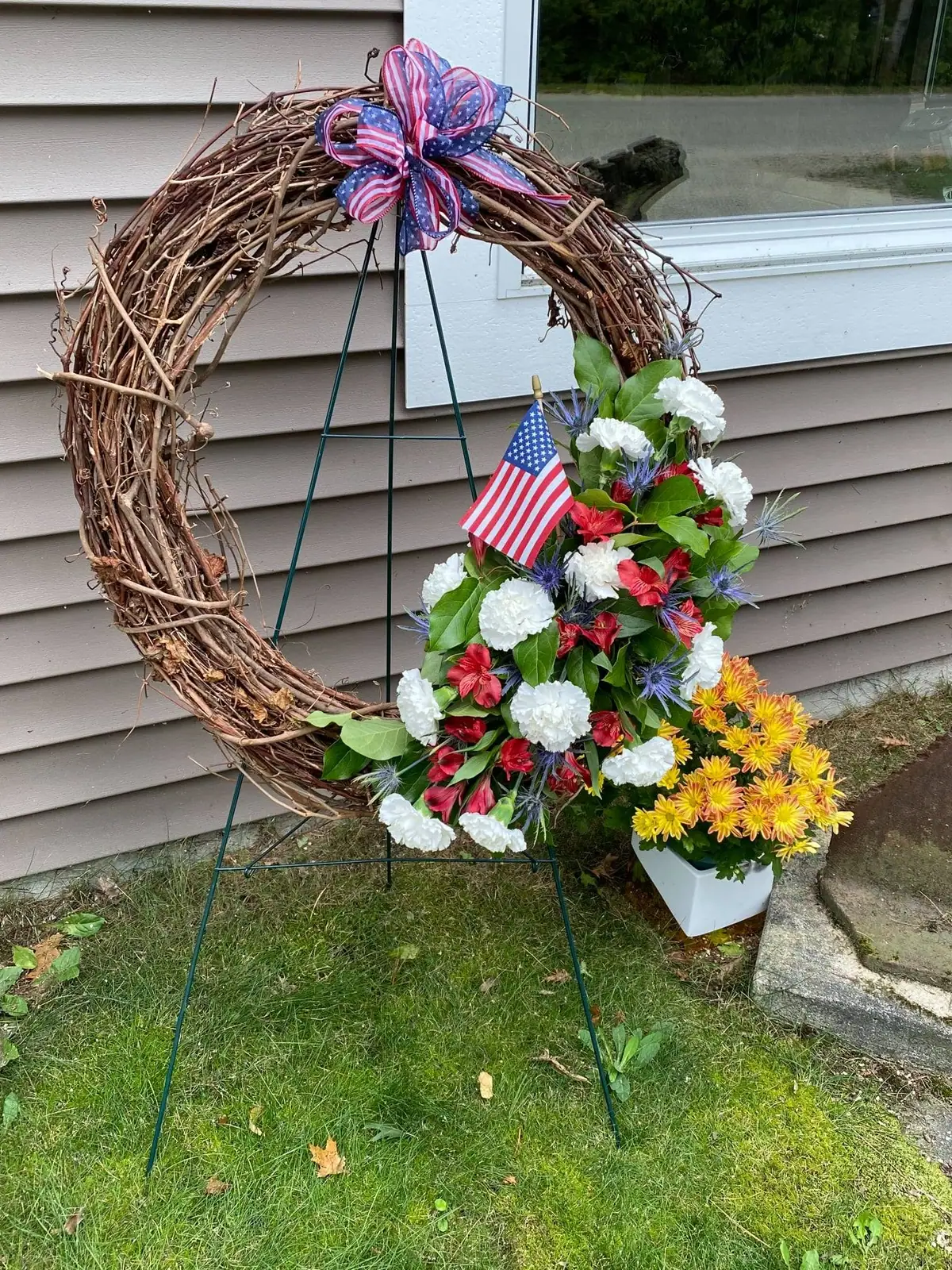 A grapevine wreath decorated with patriotic ribbons, a small American flag, and red, white, blue, and yellow flowers.