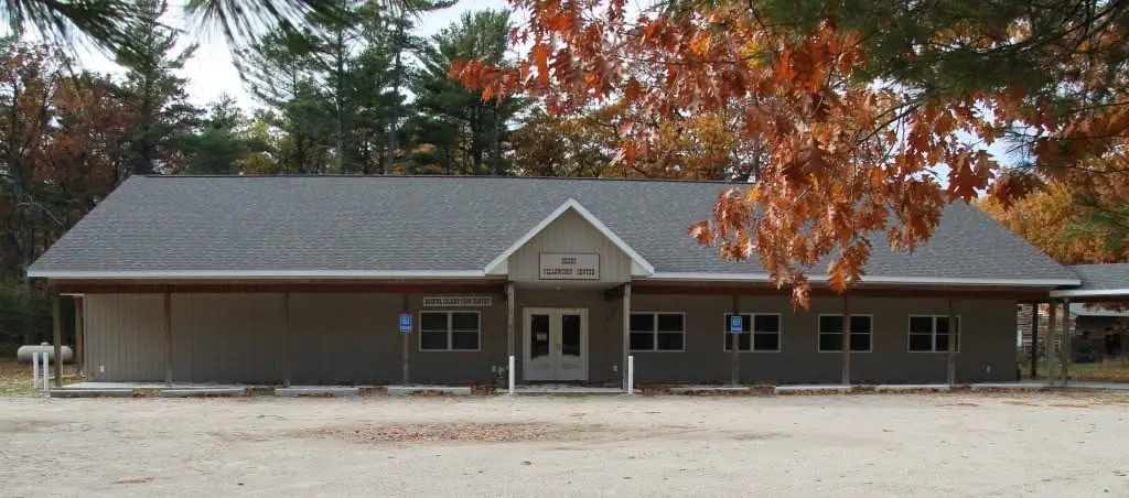 A low gray building with a central entrance, signs, surrounding trees, and orange autumn foliage.