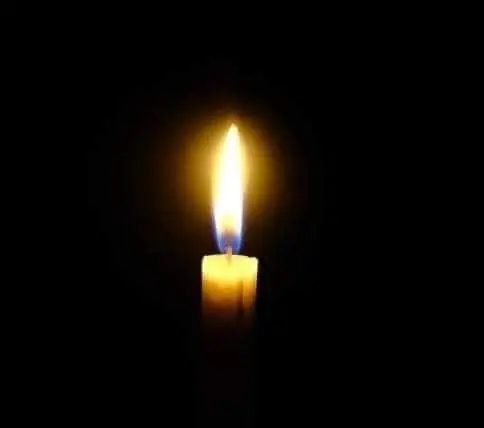A lit candle with a bright flame glows against a black background.