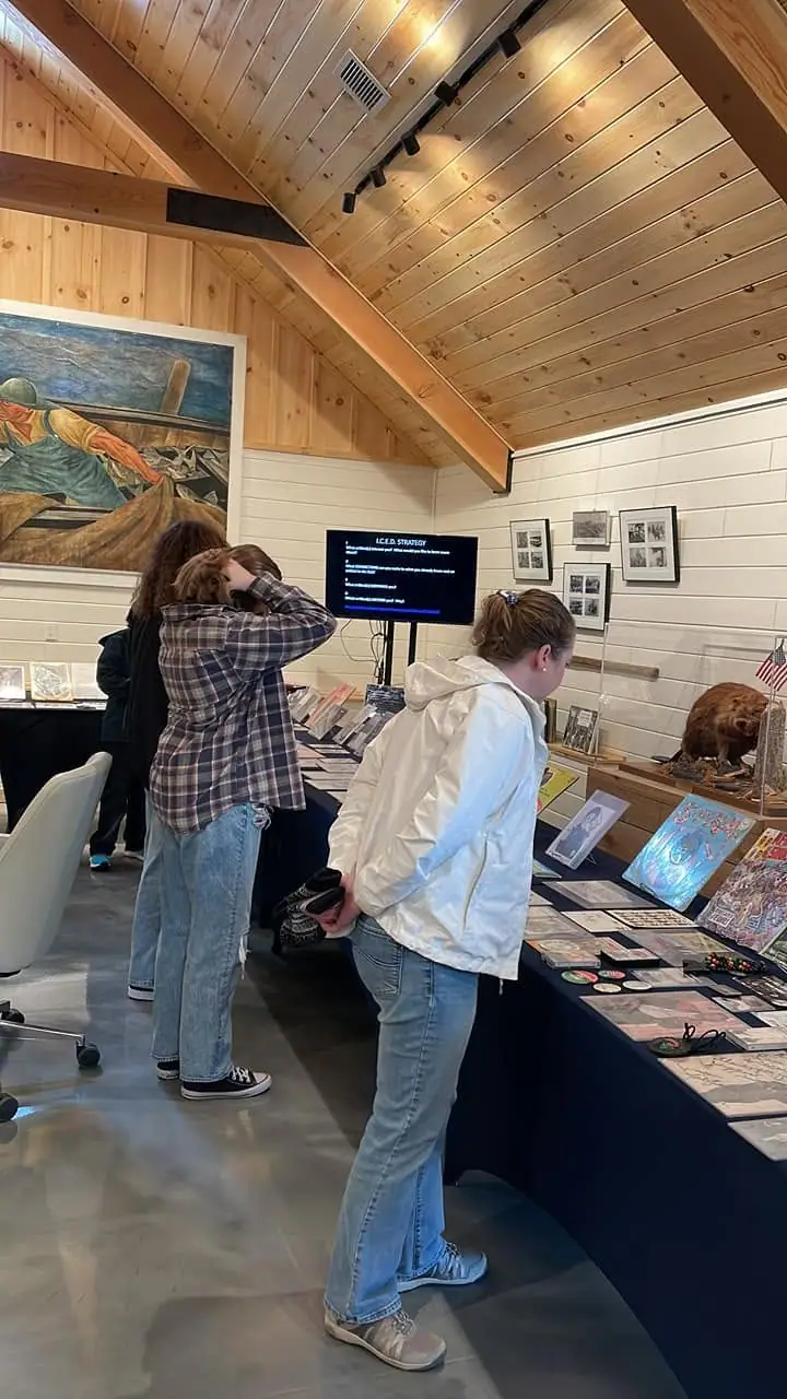 People view historical exhibits in a wood-paneled gallery with a digital display and display tables.