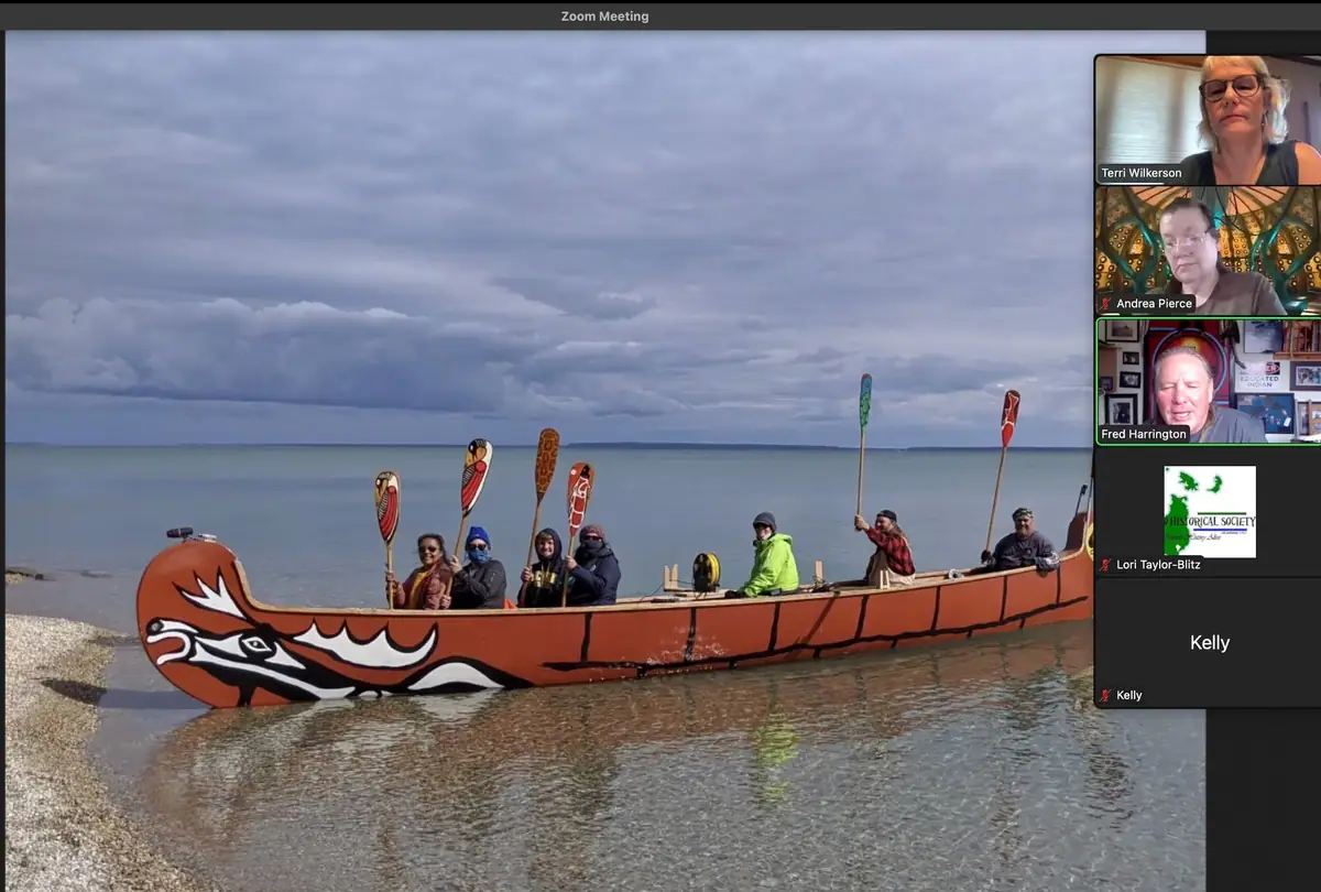 A group poses in a decorated canoe at the shoreline while a video-conference panel appears at right.
