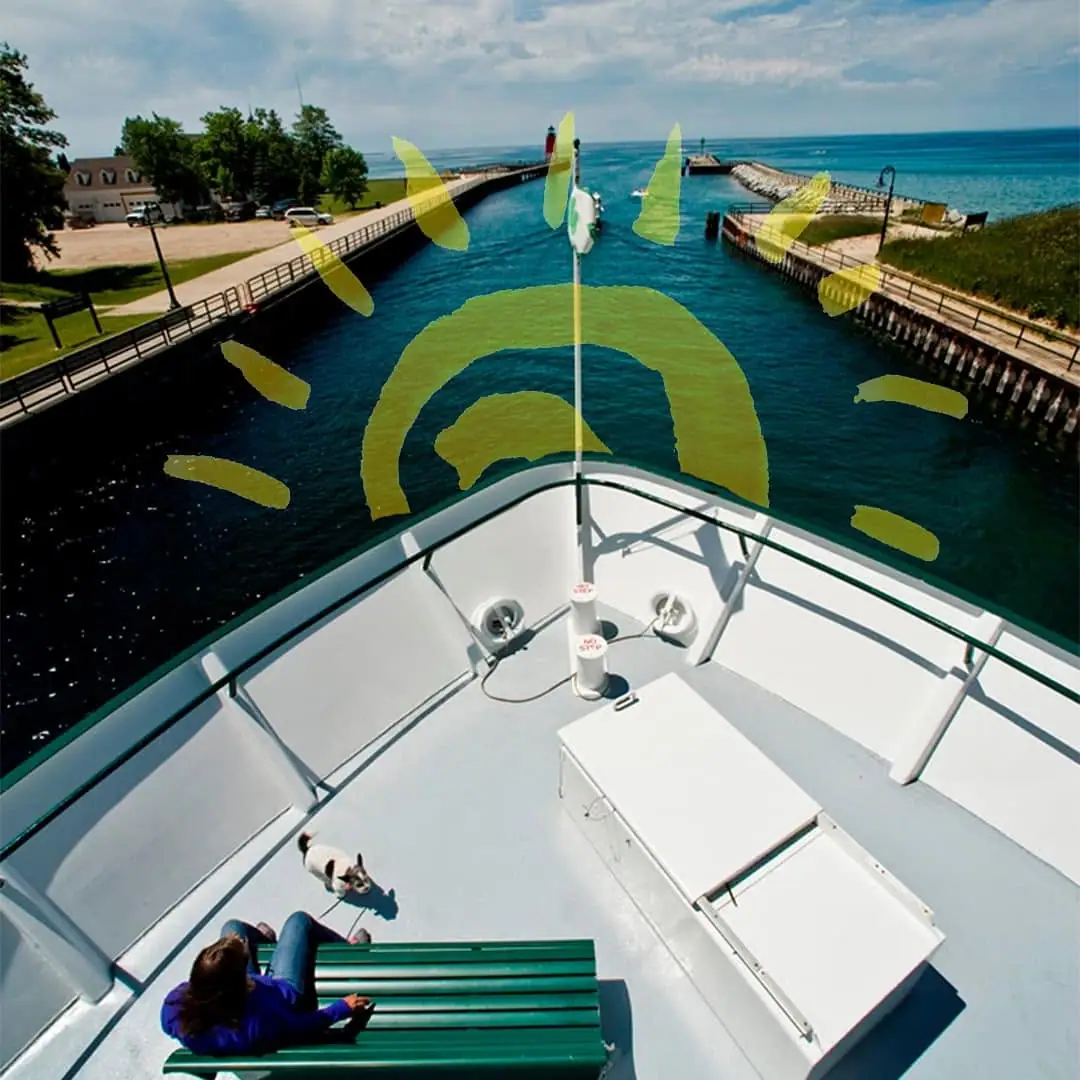 View from a ferry’s bow toward a channel, lighthouse, piers, a seated passenger, and a small dog.