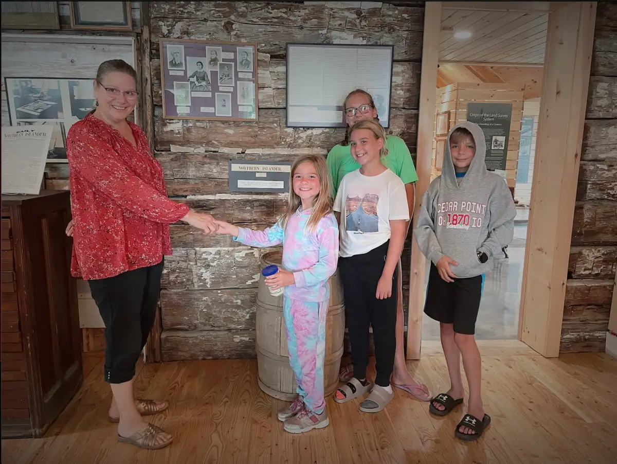 An adult and four children pose inside a museum beside historical displays and a log wall.