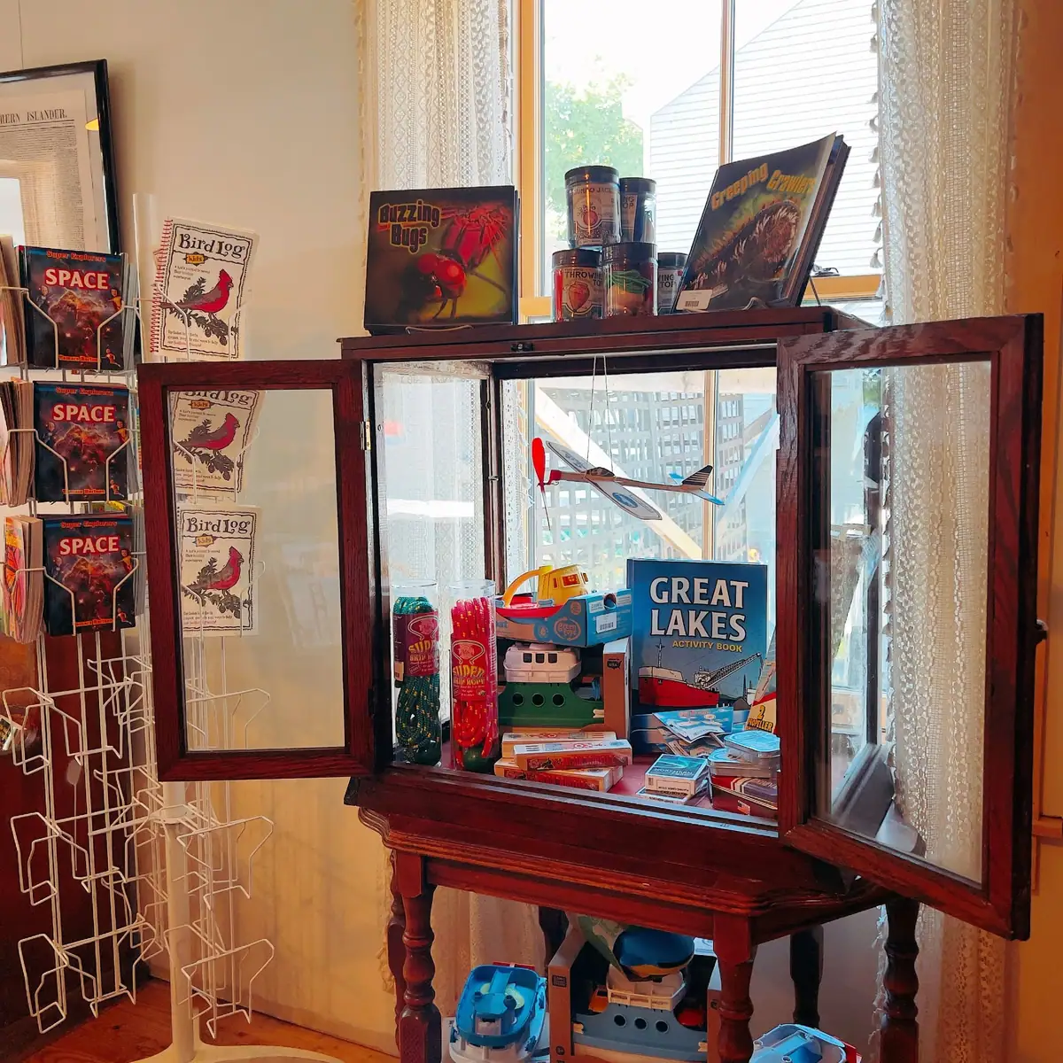 Glass-front display cabinet filled with books, toys, colorful containers, and a model airplane.