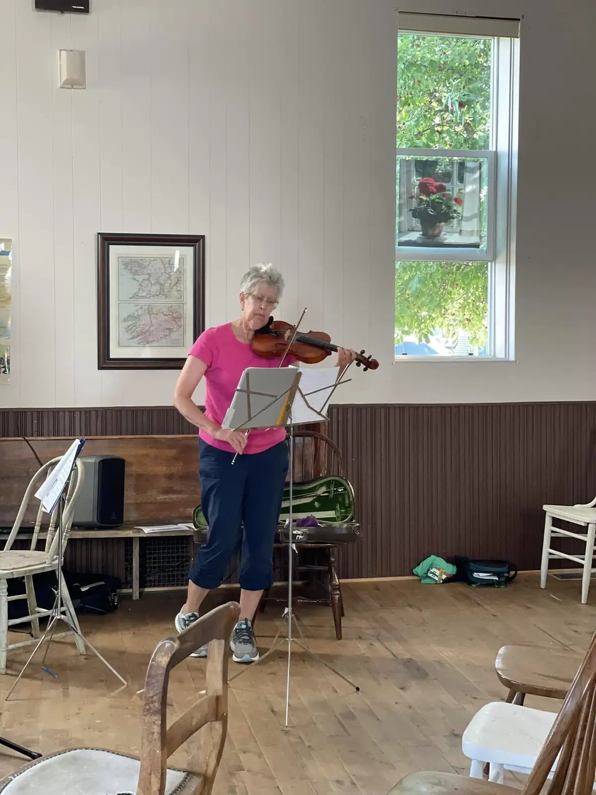 A woman plays violin beside a music stand in a wood-paneled room.