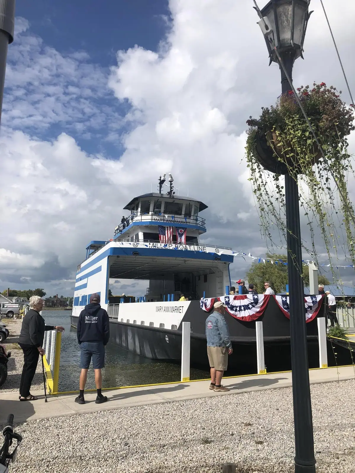 A decorated passenger ferry is moored beside a pier while several people stand nearby under a cloudy sky.