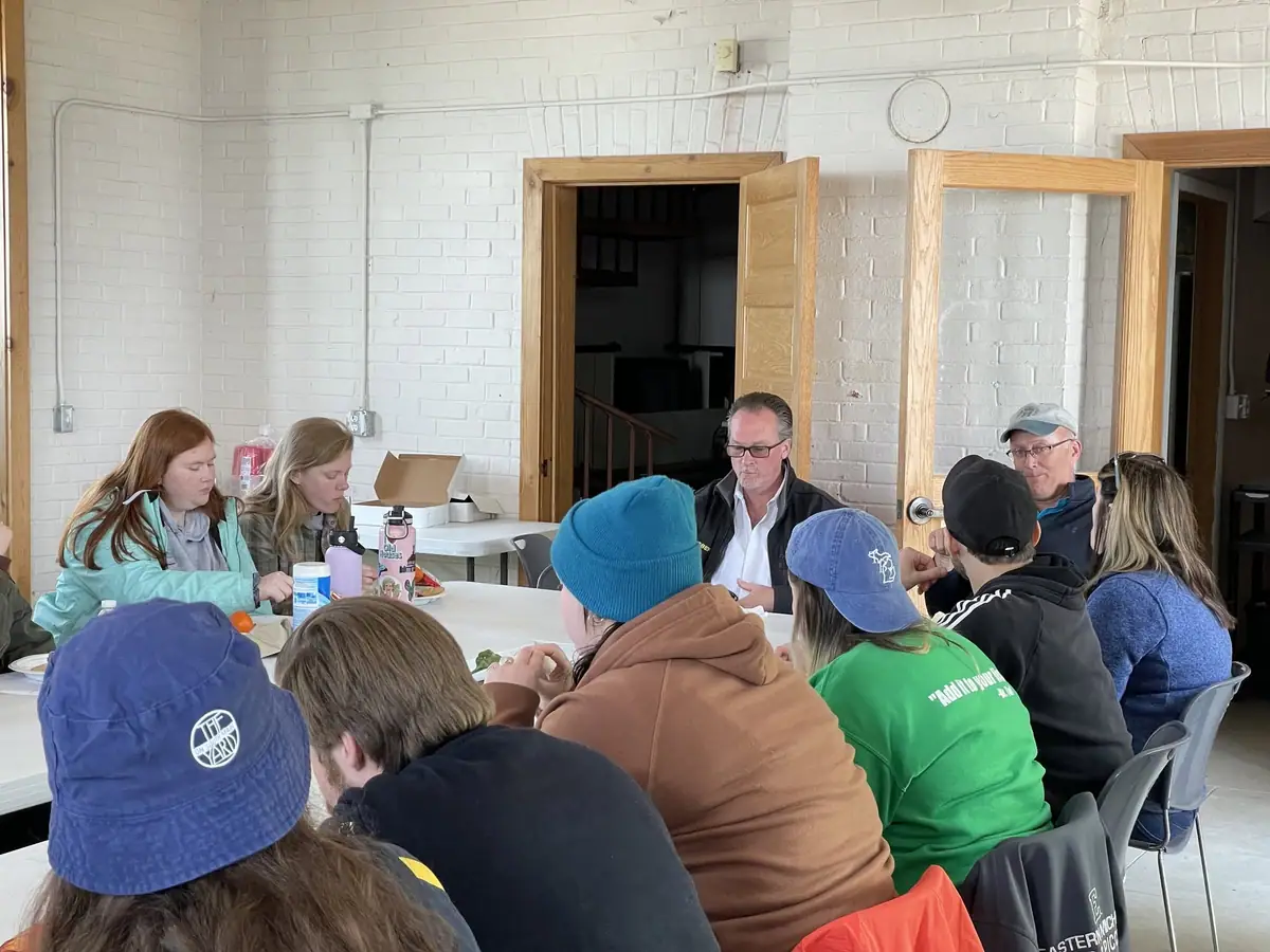 A group of people sits around a table indoors, with food and drinks spread before them.