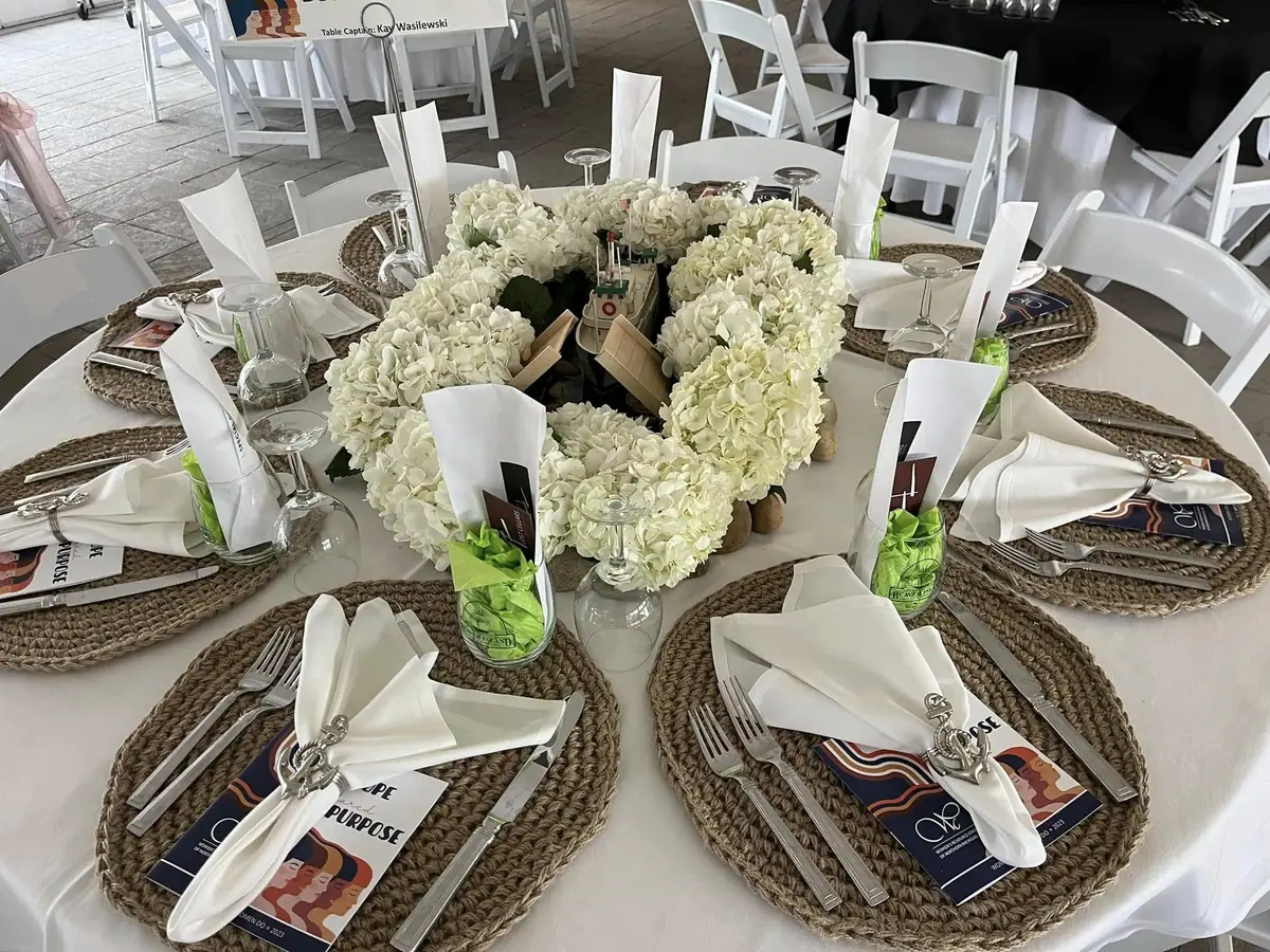 A formally set round table with white hydrangeas, a small ship model, place settings, and printed programs.