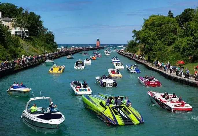 Crowded water channel filled with colorful speedboats, spectators on piers, and a lighthouse in the distance.