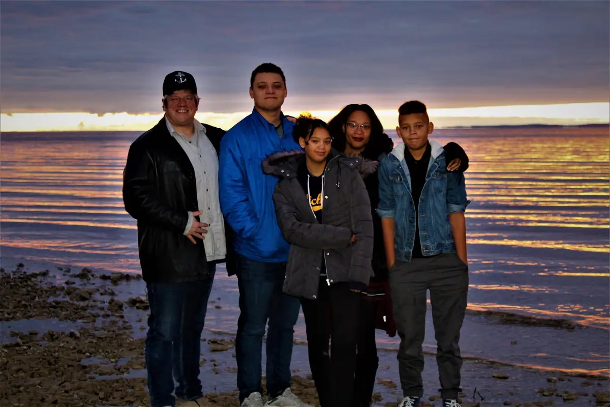 Five people stand together on a rocky shoreline at sunset.