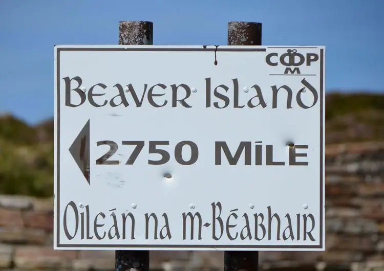 A bilingual directional sign mounted on two posts, with an arrow pointing left and a distance of 2750 miles.