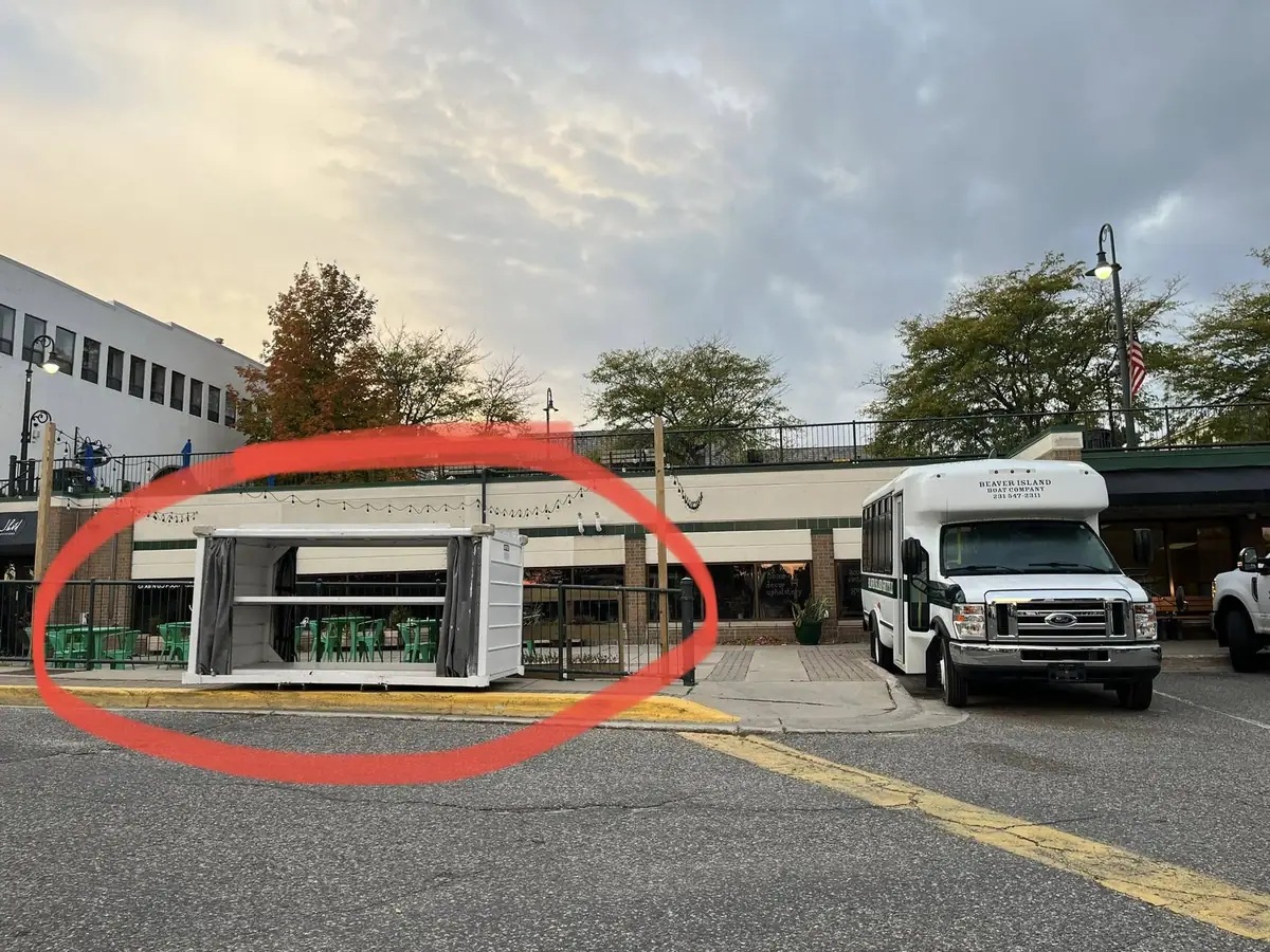 A white shuttle bus is parked beside a covered outdoor seating enclosure on a commercial street.