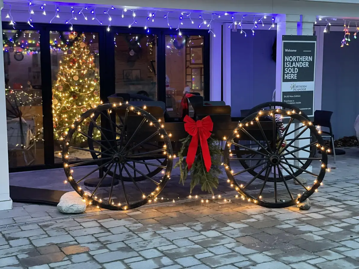 A storefront decorated with lit wagon wheels, a red bow, greenery, and a Christmas tree.