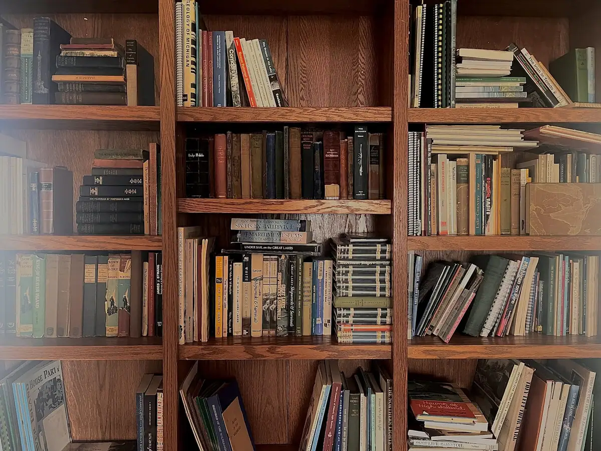 A wooden bookcase filled with upright, stacked, and leaning books, several with readable titles on their spines.