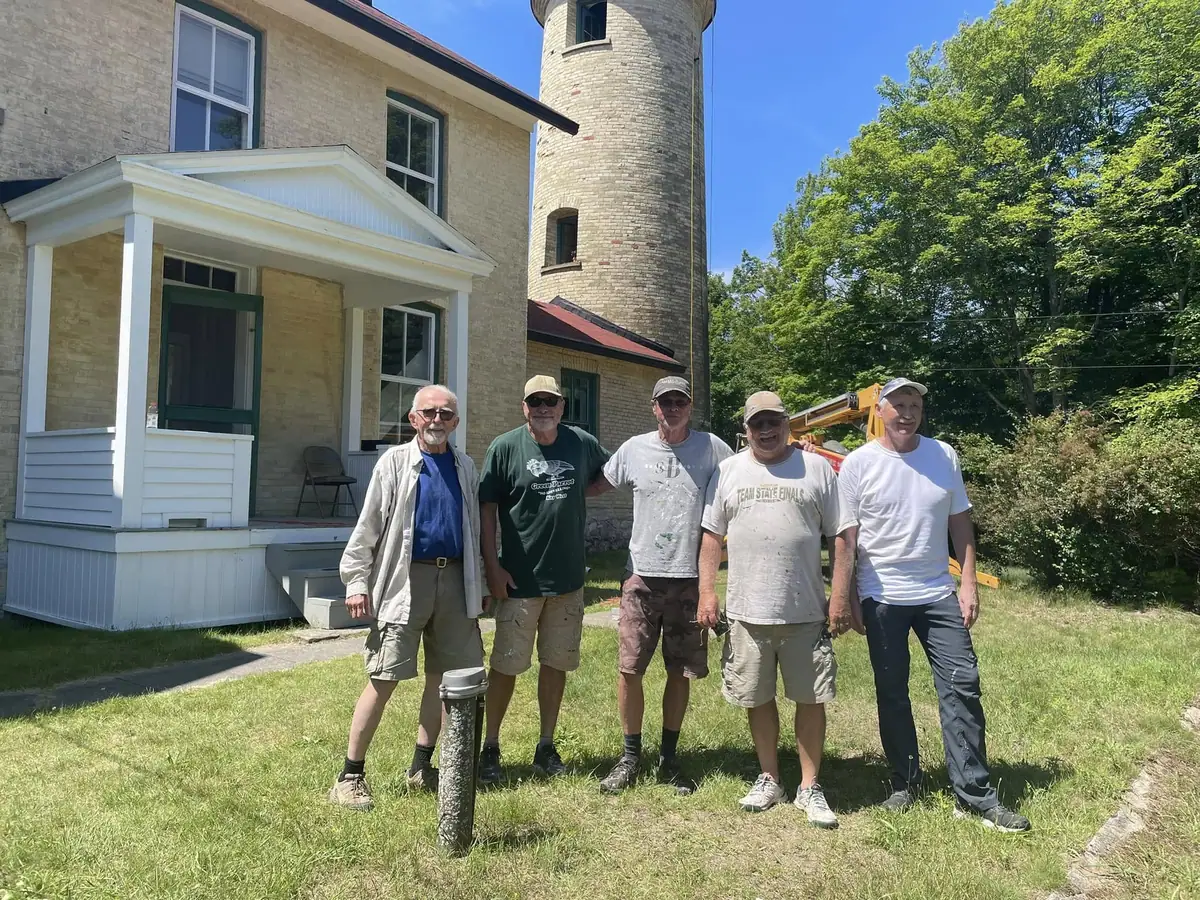 Five men pose on a lawn beside a brick building and cylindrical tower.